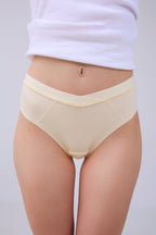 A model wearing a pair of light beige high-waisted briefs with a V-front waistband, paired with a white ribbed top, shown from the waist down against a light gray background.